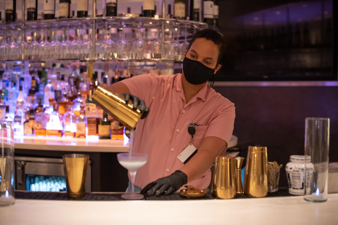 A bartender wearing a facemask and gloves pours a cocktail at the bar at Hotel Zena in DC