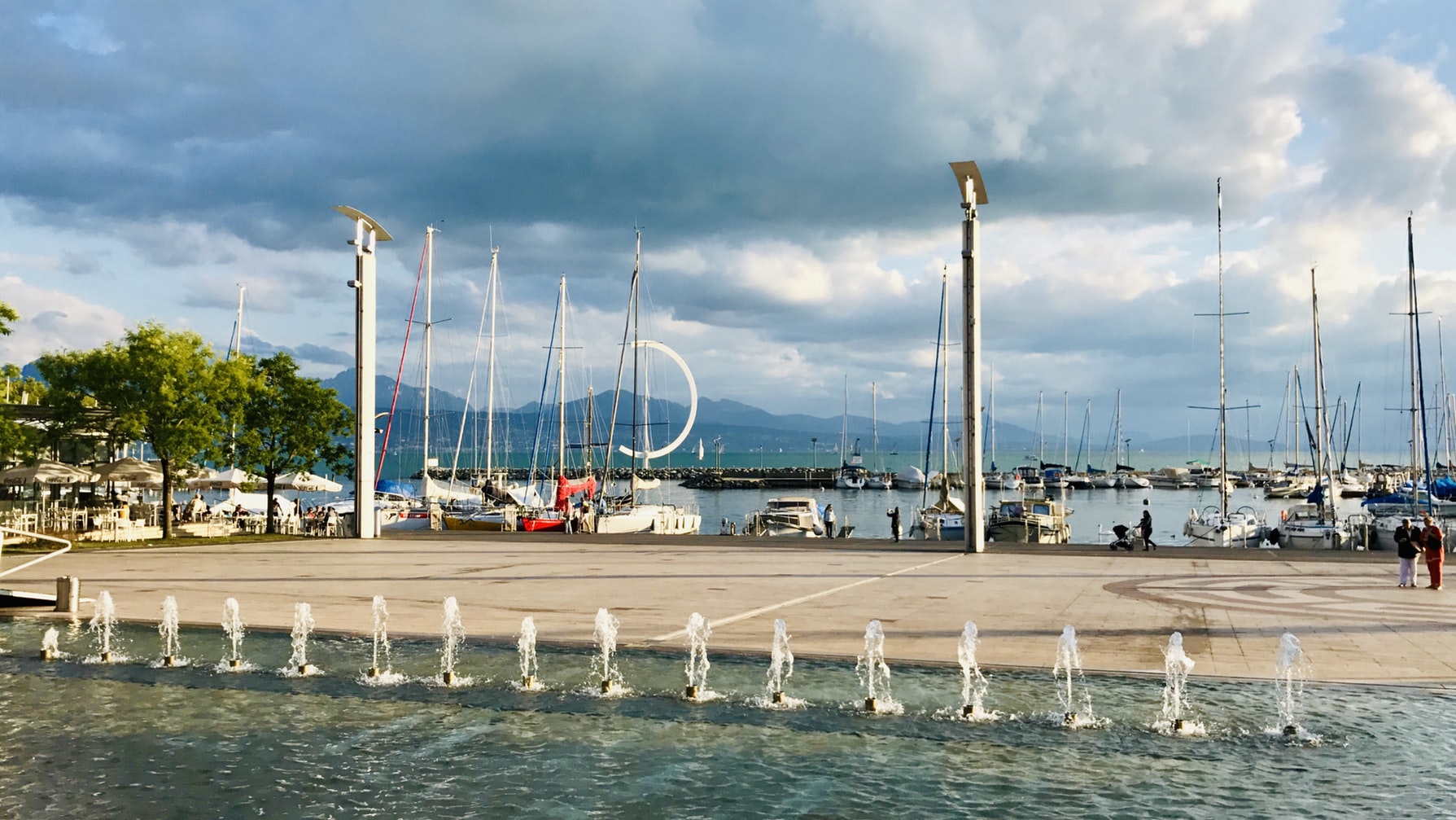 view of the harbor in Lausanne with boat masts and a fountain in the foreground