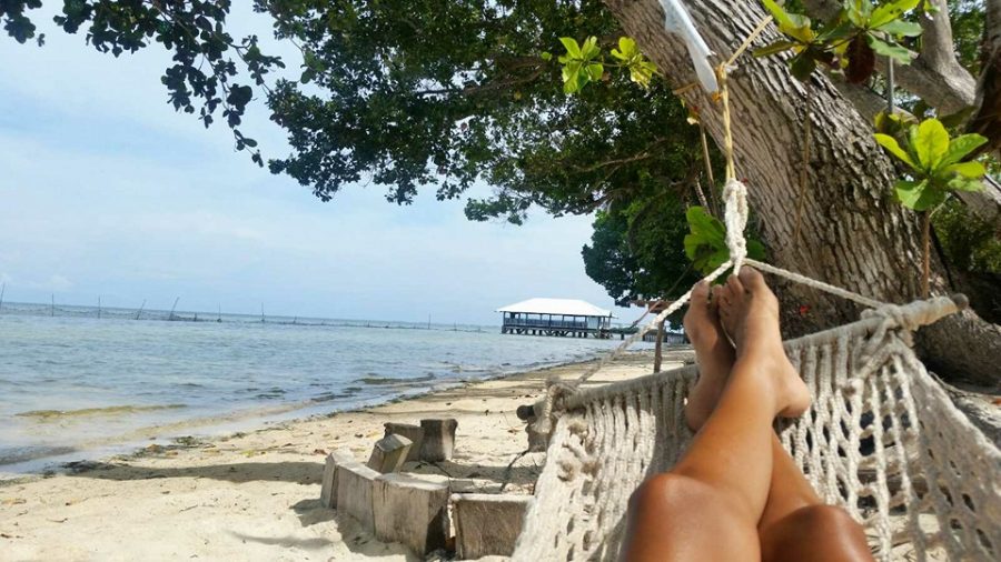 Image of a person\'s legs and feet relaxing on a hammock on the beach