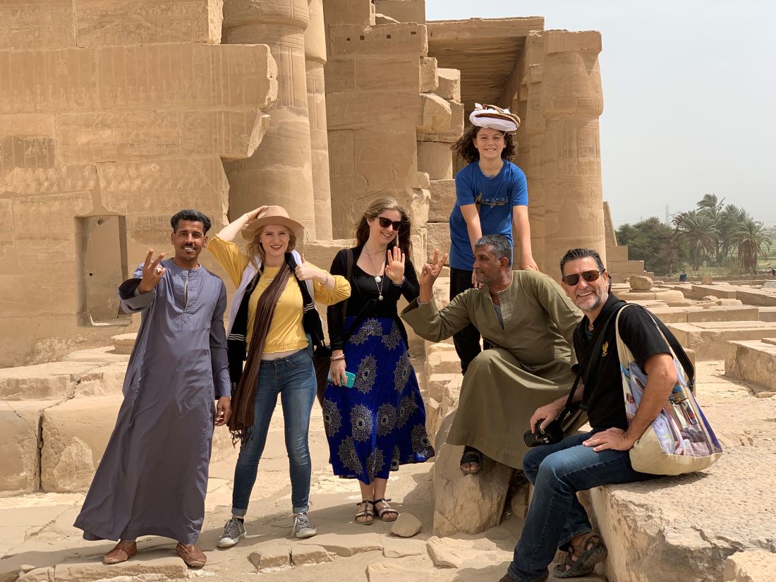 A family visiting Egypt and posing with two local tour guides showing peace signs