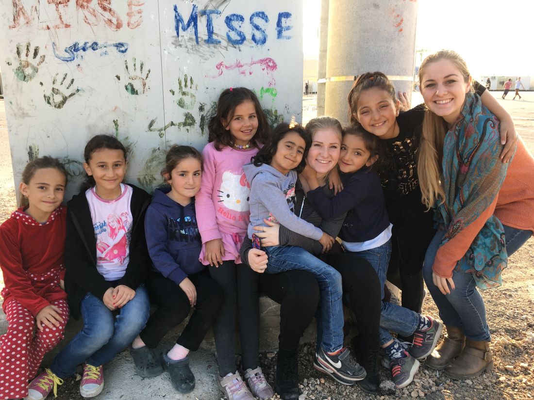 Kaitlin Murray of Odyssey HQ posing with young kids in a refugee camp where she volunteered