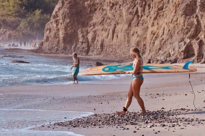 Chel Rogerson carrying her surfboard towards the sea along the beach in Mexico