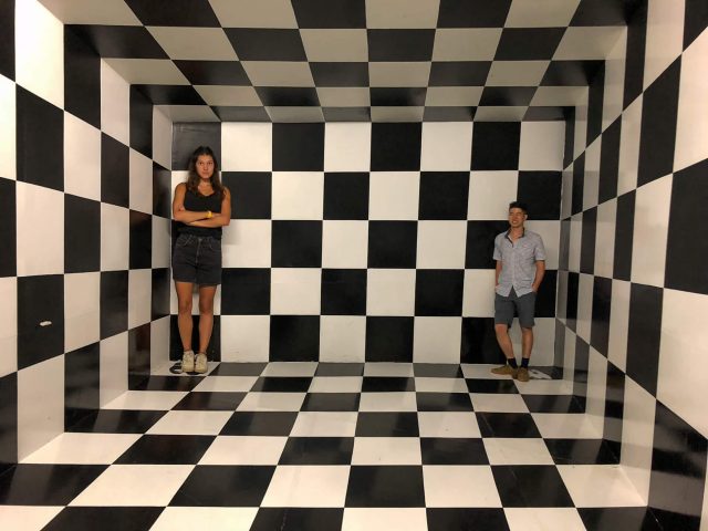 A woman and a man in a black and white checkered room like an optical illusion