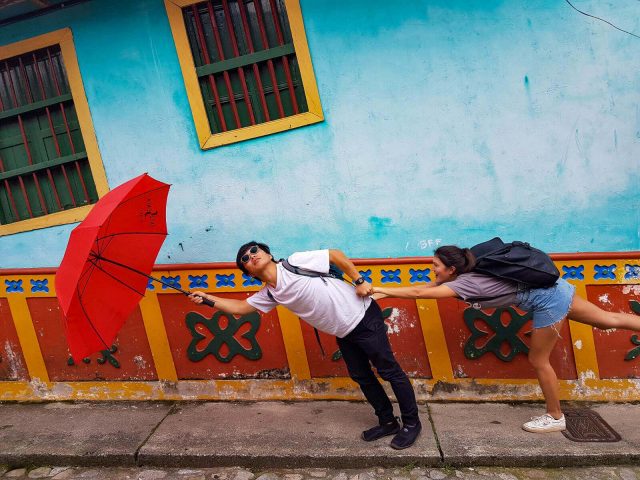 Man holding a red umbrella and a woman\'s hand, looking like they\'re being blown away in Guatape
