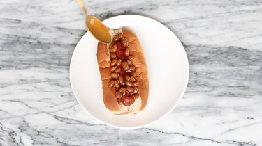 Spooning Boston baked beans on top of hot dog