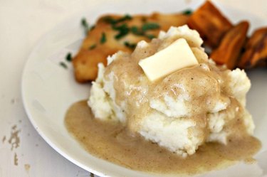 A plate of food including mashed potatoes covered in gravy and a pat of butter