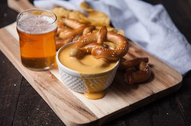 A wooden tray with a bowl of cheese sauce, soft pretzels and beer