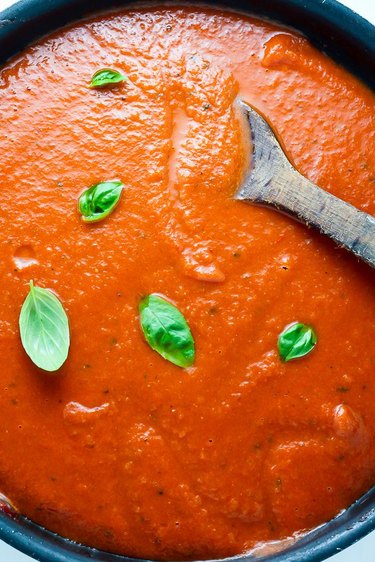Close up image of red sauce, with basil leaves and wooden spoon
