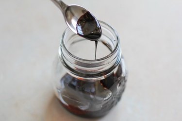 A spoonful of balsamic reduction sauce pouring into a jar