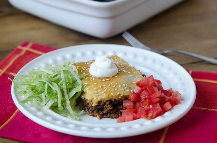 A baked taco square beside shredded lettuce, diced tomatoes and a dollop of sour cream.