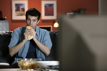 Man eating sandwich and watching television