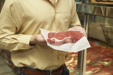 Mid section view of a person holding a raw steak in a supermarket