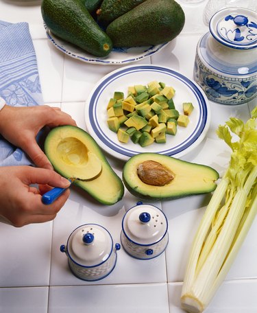 close-up of hands scooping the flesh from an avocado on a tiled counter